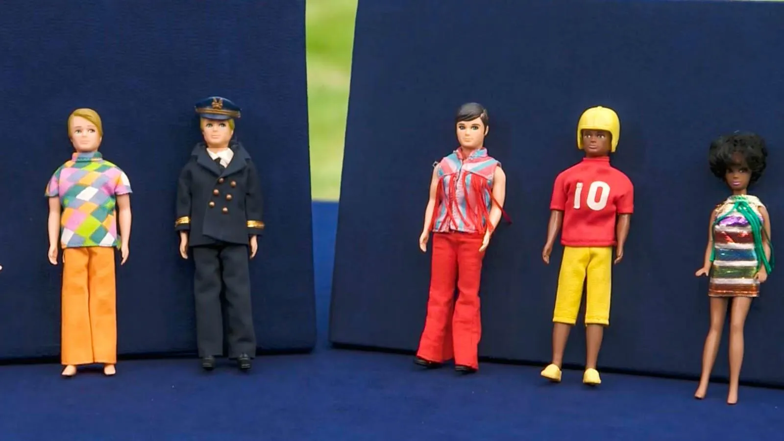 Five dolls of various ethnicities and occupations lie agains a blue backdrop.