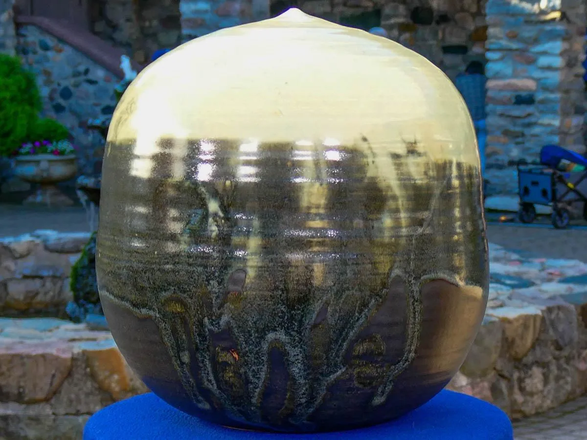 A spherical stoneware pot with a gradient from white to dark grey sits on top of a blue table.