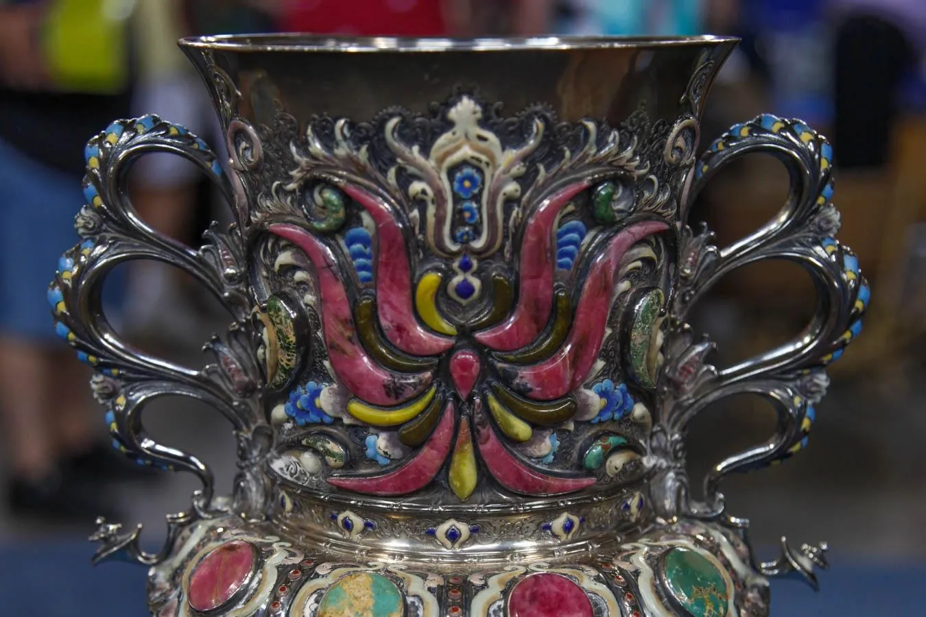 Close up of sterling vase with enamel designs on neck and circular turquoise stones on body.