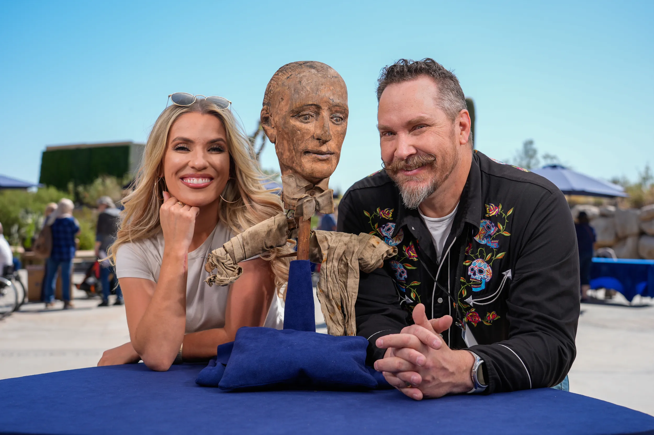 Appraiser James Supp and ROADSHOW guest lean in close to the camera, on either side of a head statue that was brought to be appraised
