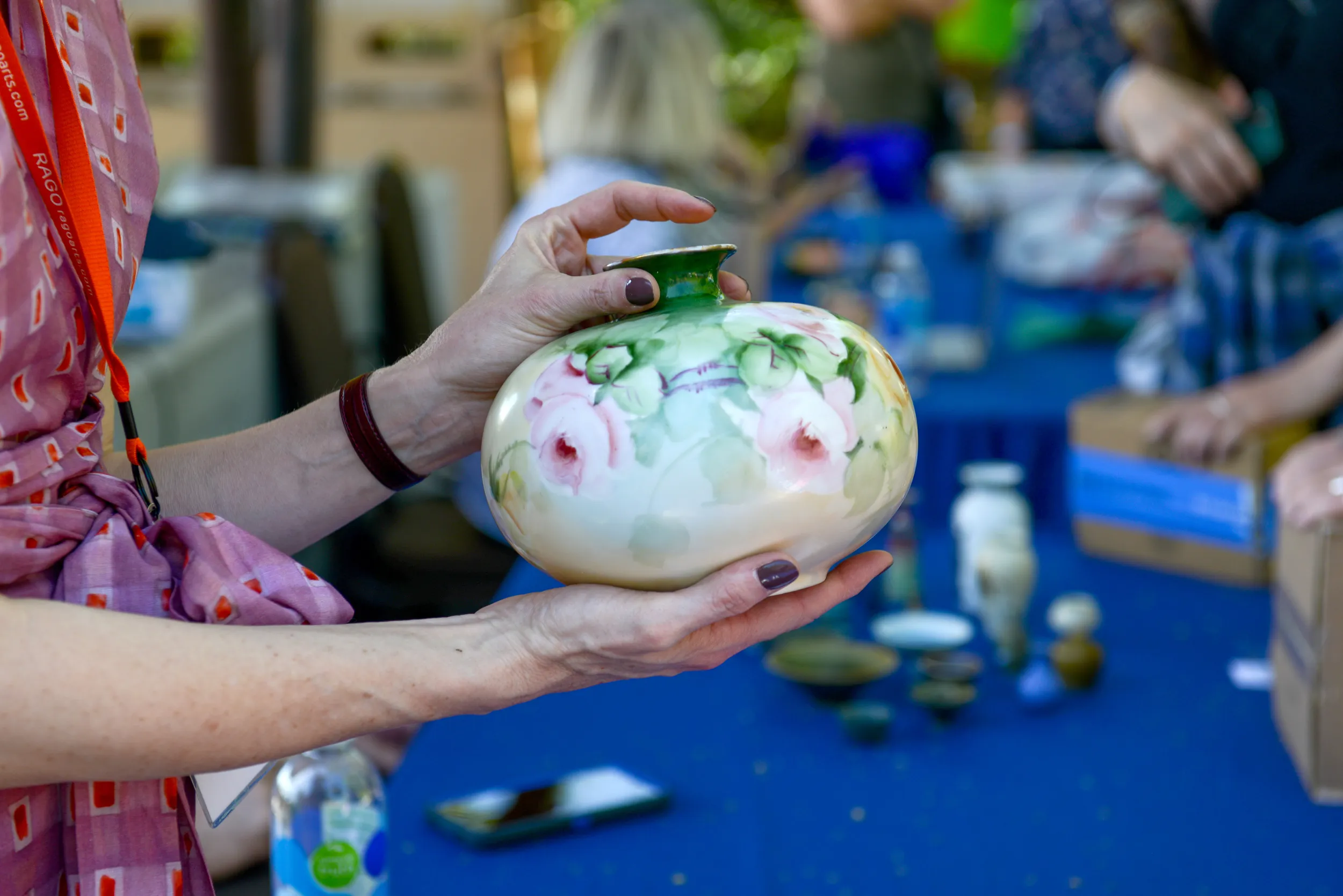 Close-up of a round glass vase, decorated in pink flowers and rich green leaves around the mouth of the vase.