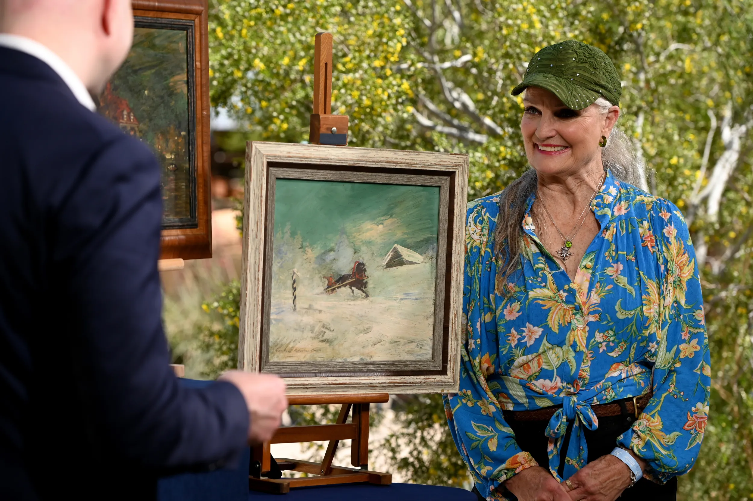 A woman smiles at an appraiser as he speaks to her painting while filming an on-camera appraisal.