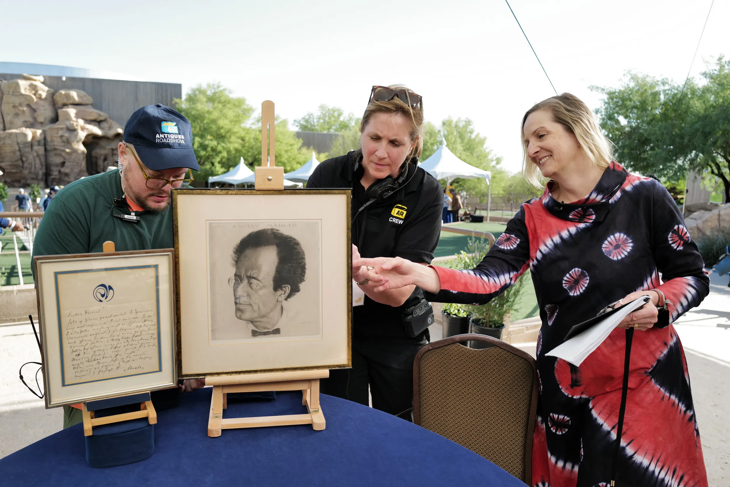 A framed sketch and letter are carefully set-up to be filmed by a ROADSHOW director, scenics staff, and appraiser.