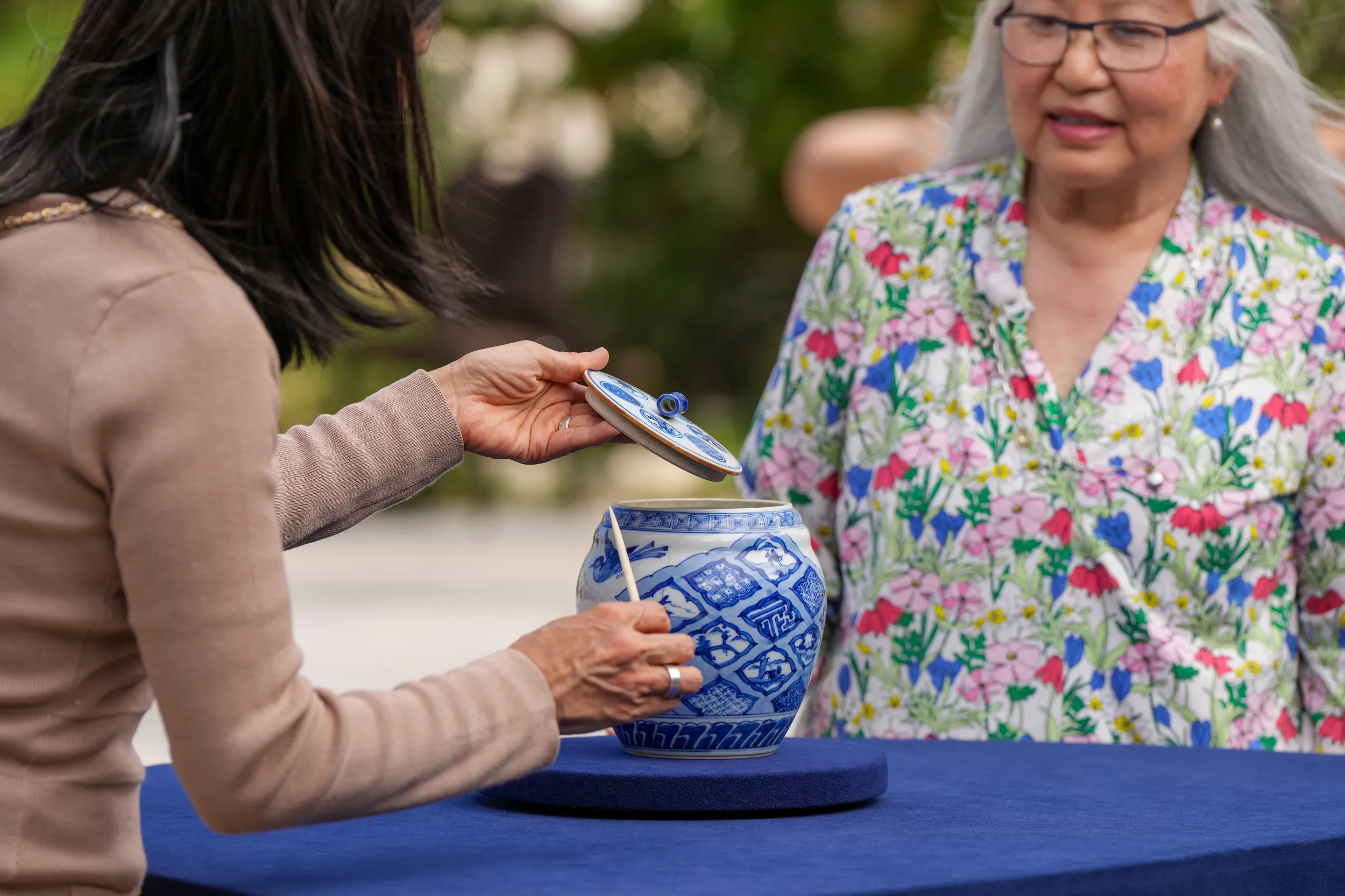 An appraiser lifts the lid on a white stoneware vase with blue birds and squares on an appraisal table as it's filmed.