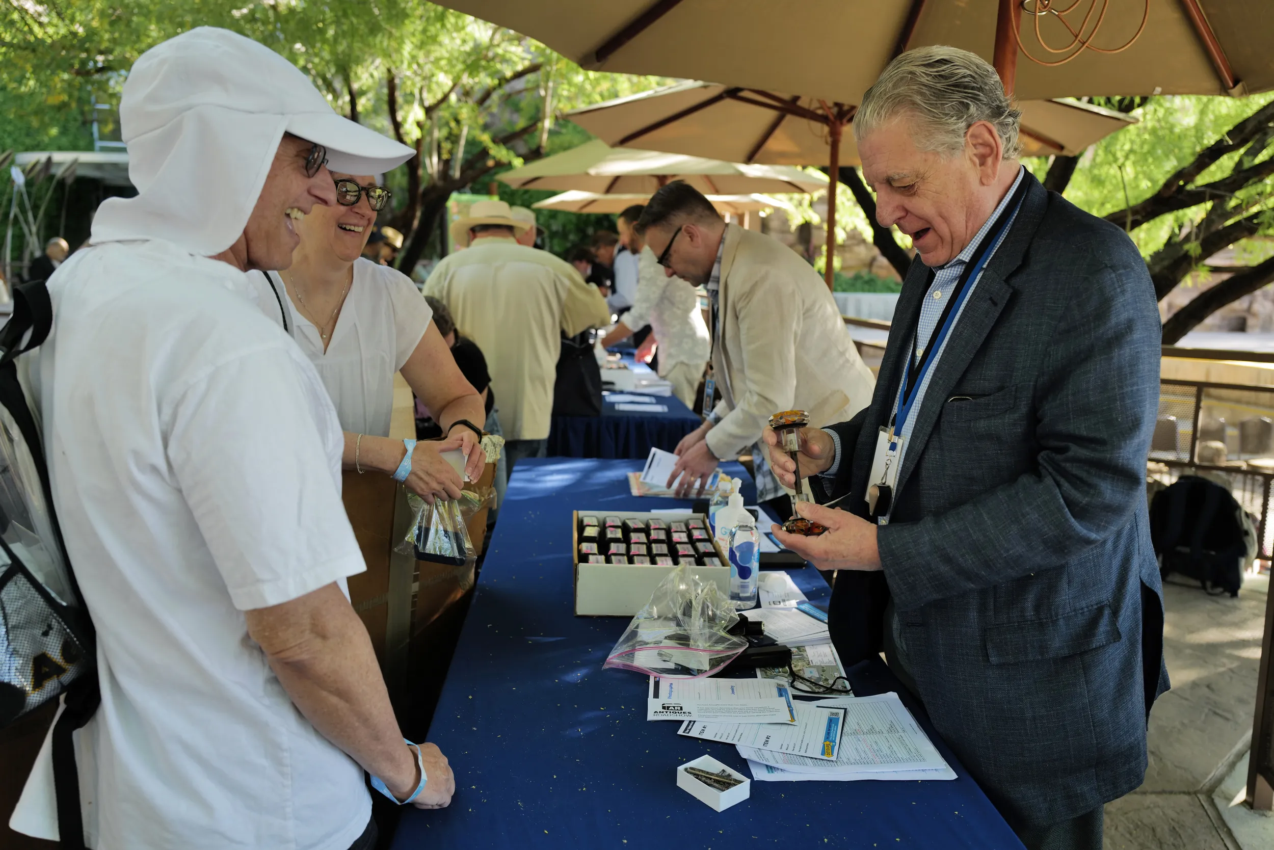 A triage appraiser smiles at a glass item brought in by two happy guests.