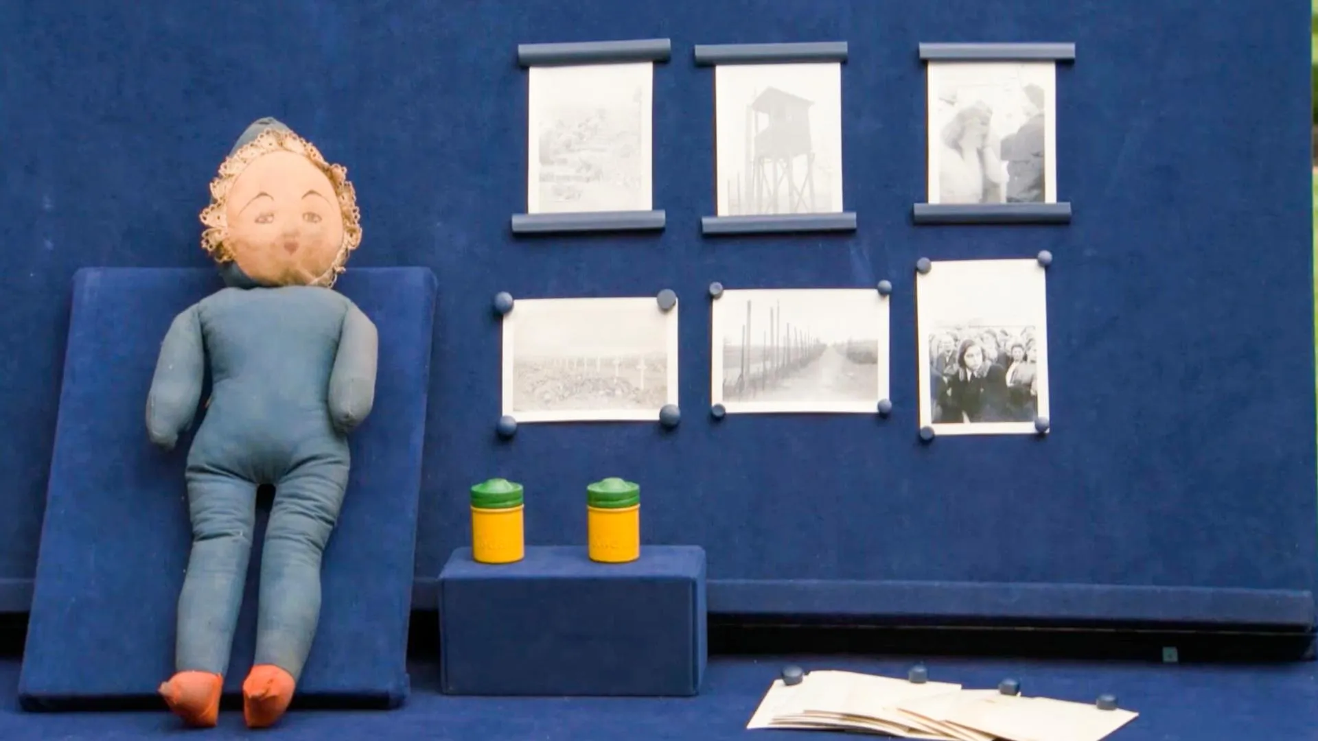 A doll, placed on a blue display board next to photographs and film canisters on a blue table.