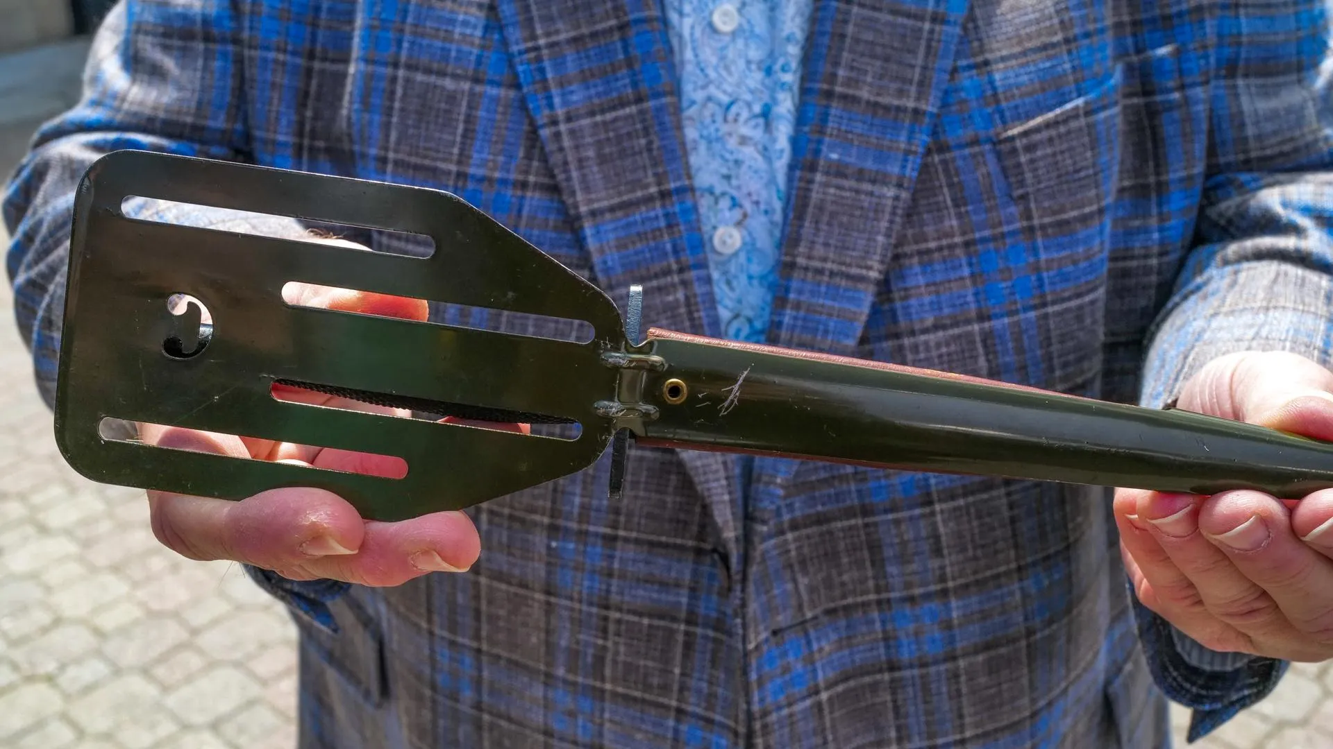 A person holds a black pancake flipper with a pointed end covered in sheath.