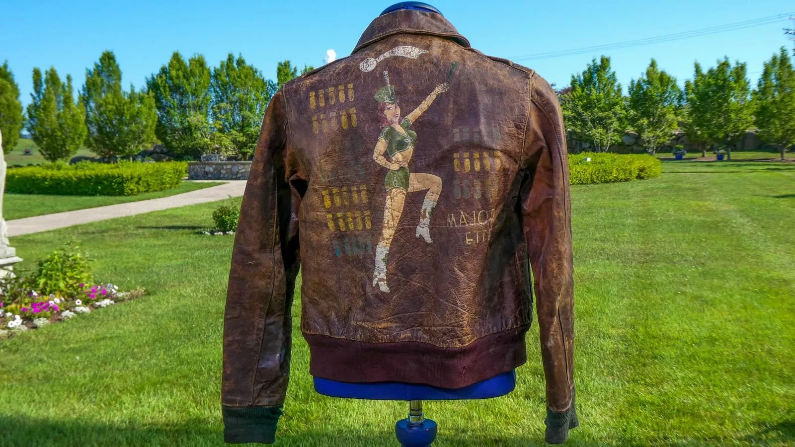 A brown jacket on maniquin with a army majorette painted on the back.