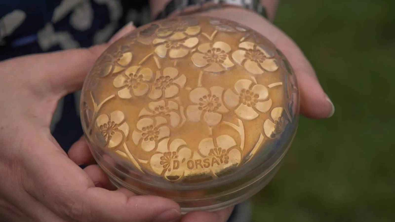 Close up of two hands holding a powder jar decorated with floral details.