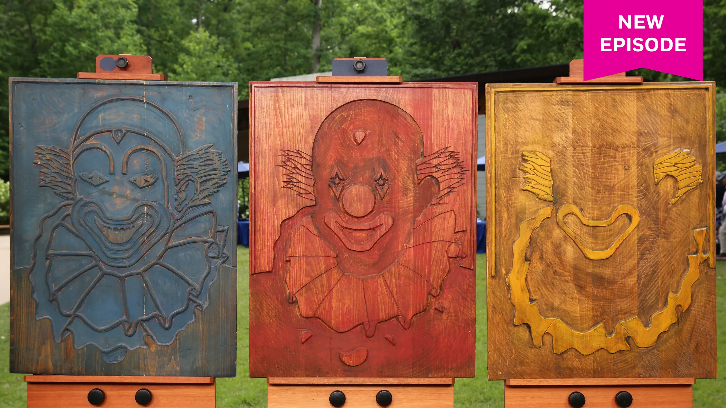 Three large wooden block signs of clowns. From left to right they're stained in blue, red, and yellow paint.