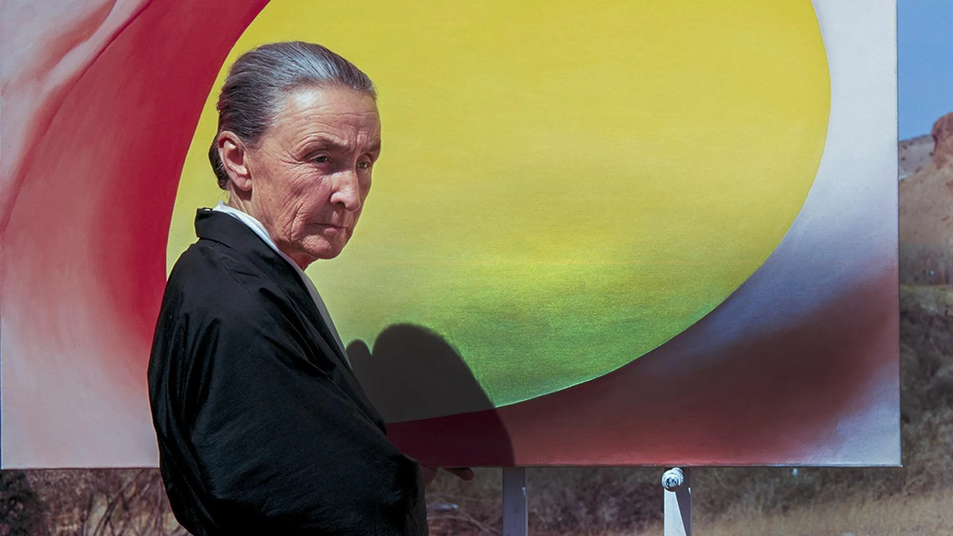 Color photograph of artist George O'Keefe standing in front of a painting