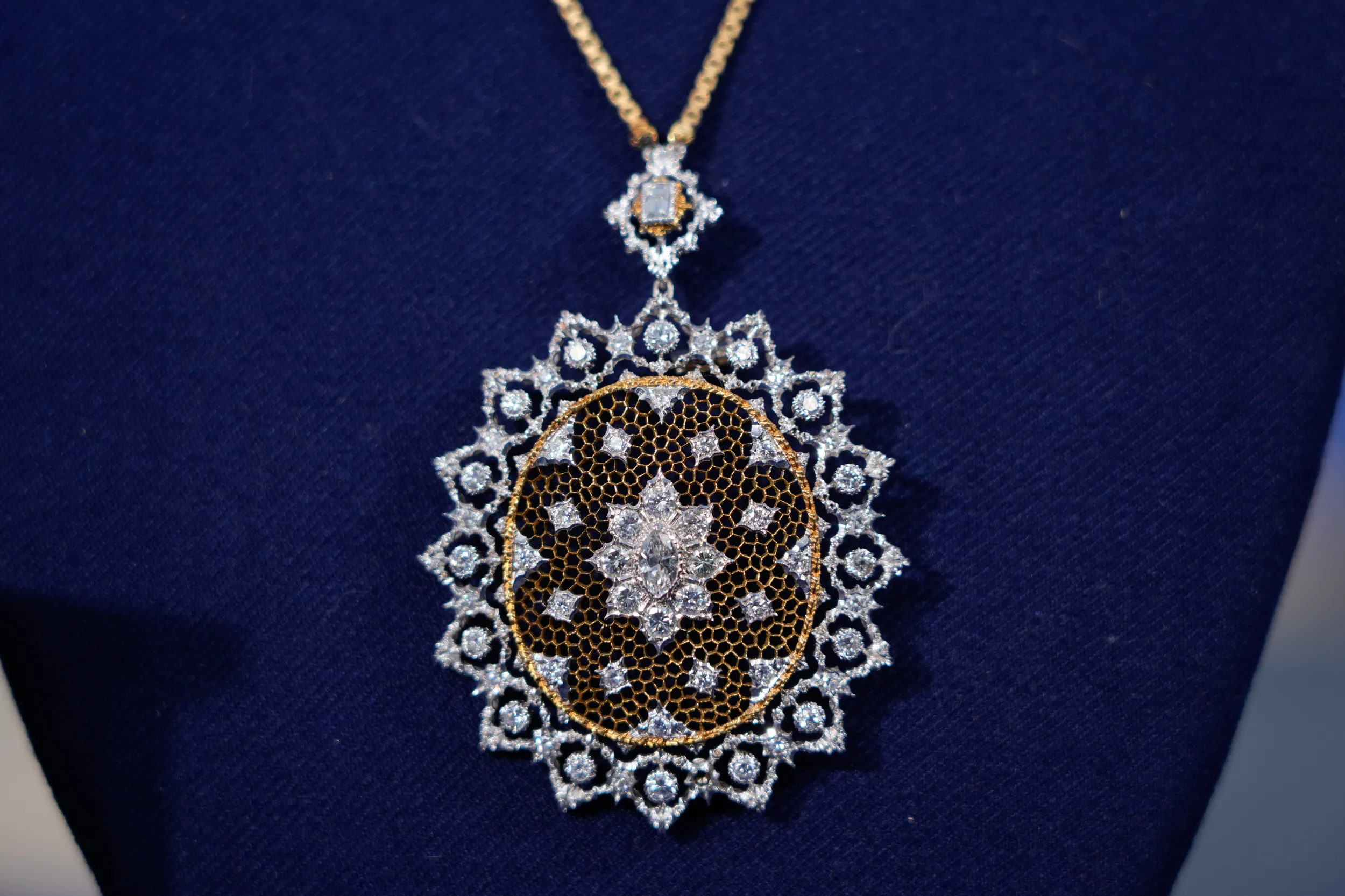 Close up of a necklace pendant made of tiny circles of gold to form a circle. It's surrounded by circular diamonds all around, inside silver circles. In the center is a large diamond.