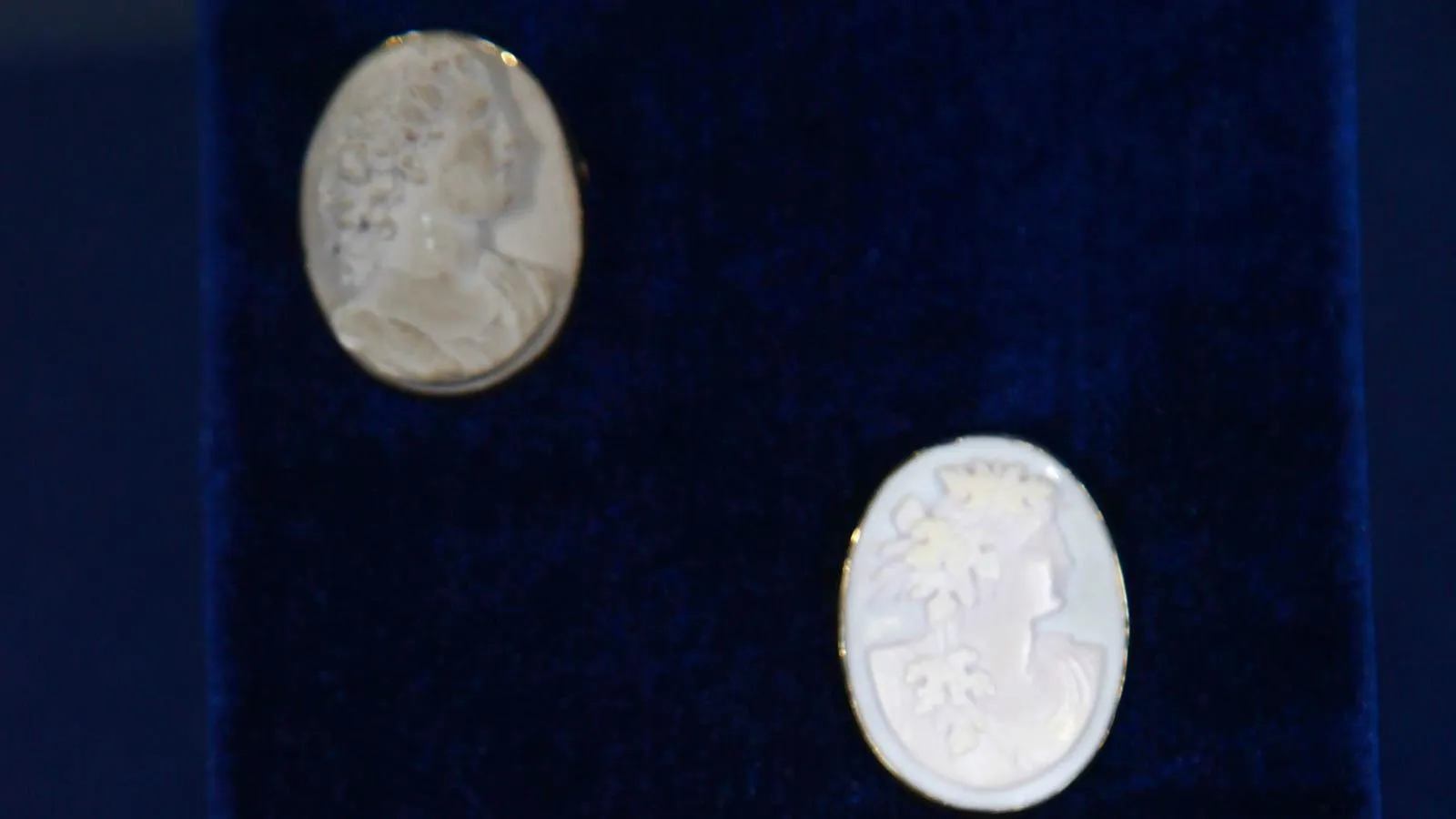Close up of two cameos that have carved portraits of a woman.