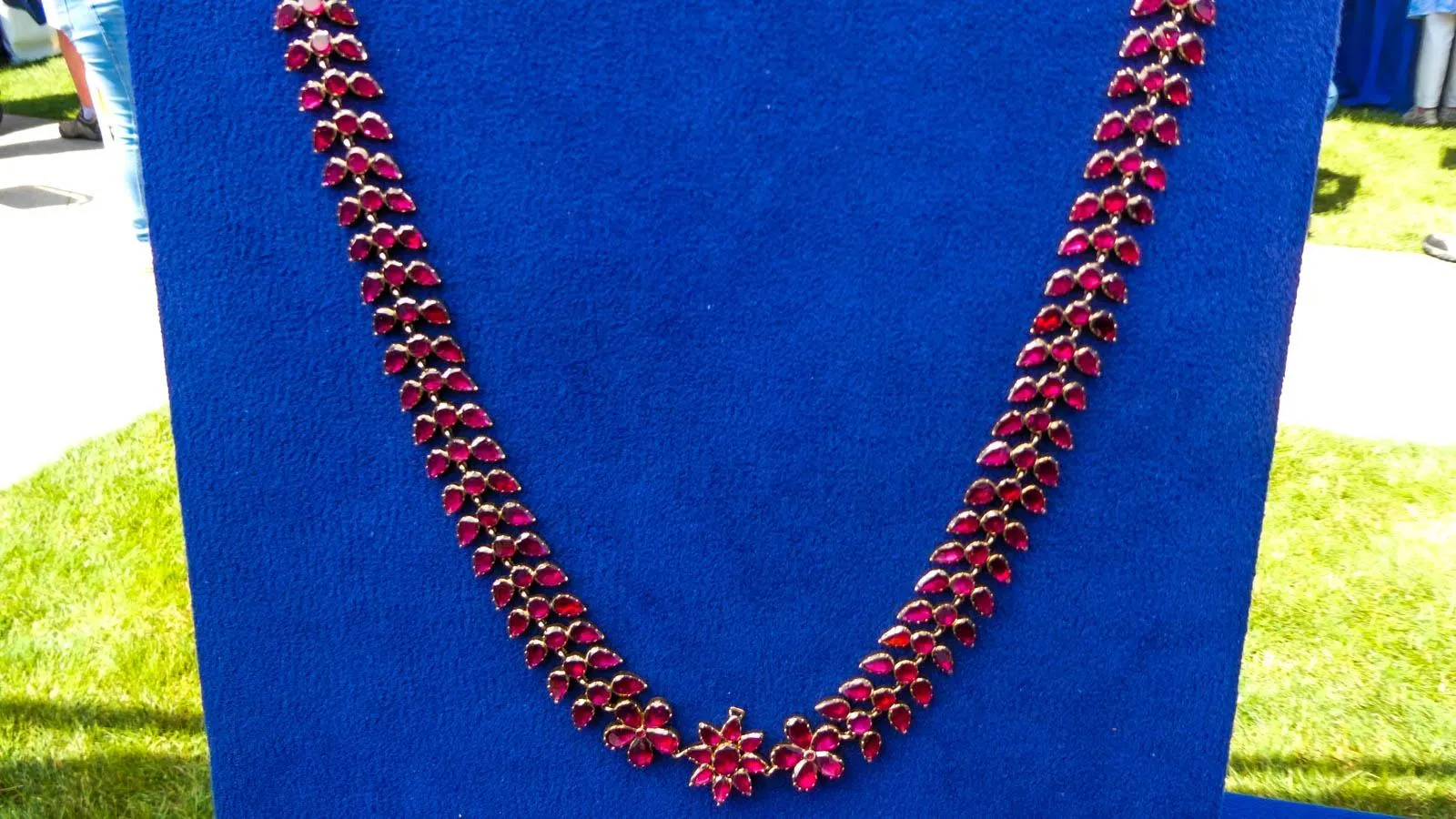 Close up of a red necklace in a leaflike pattern drapped around a blue neck form.