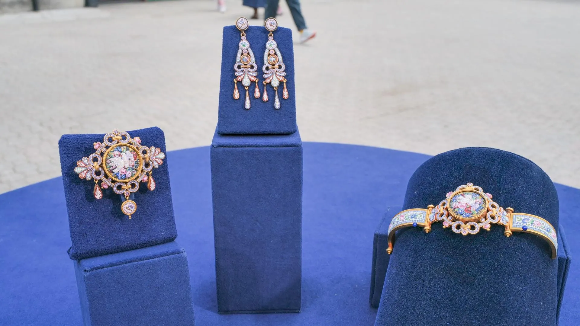 A matching set of a bracelet, earrings, and a brooch of various colors and bird themes sits on top of blue display stands.
