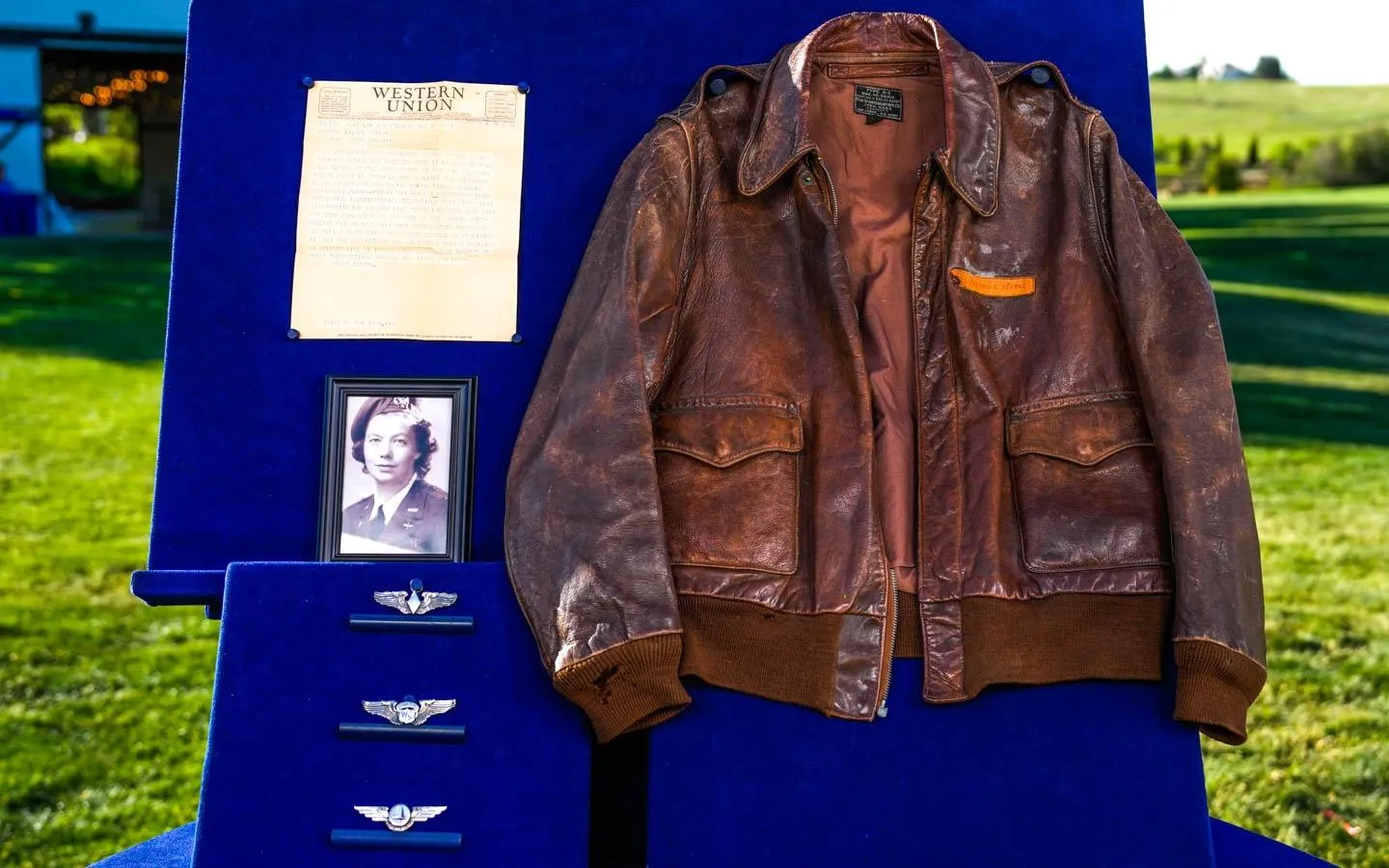 A Women Airforce Service Pilots collection, which includes a telegram, a framed monochromatic portrait of pilot, three pilot wings, and a dark brown leather jacket.