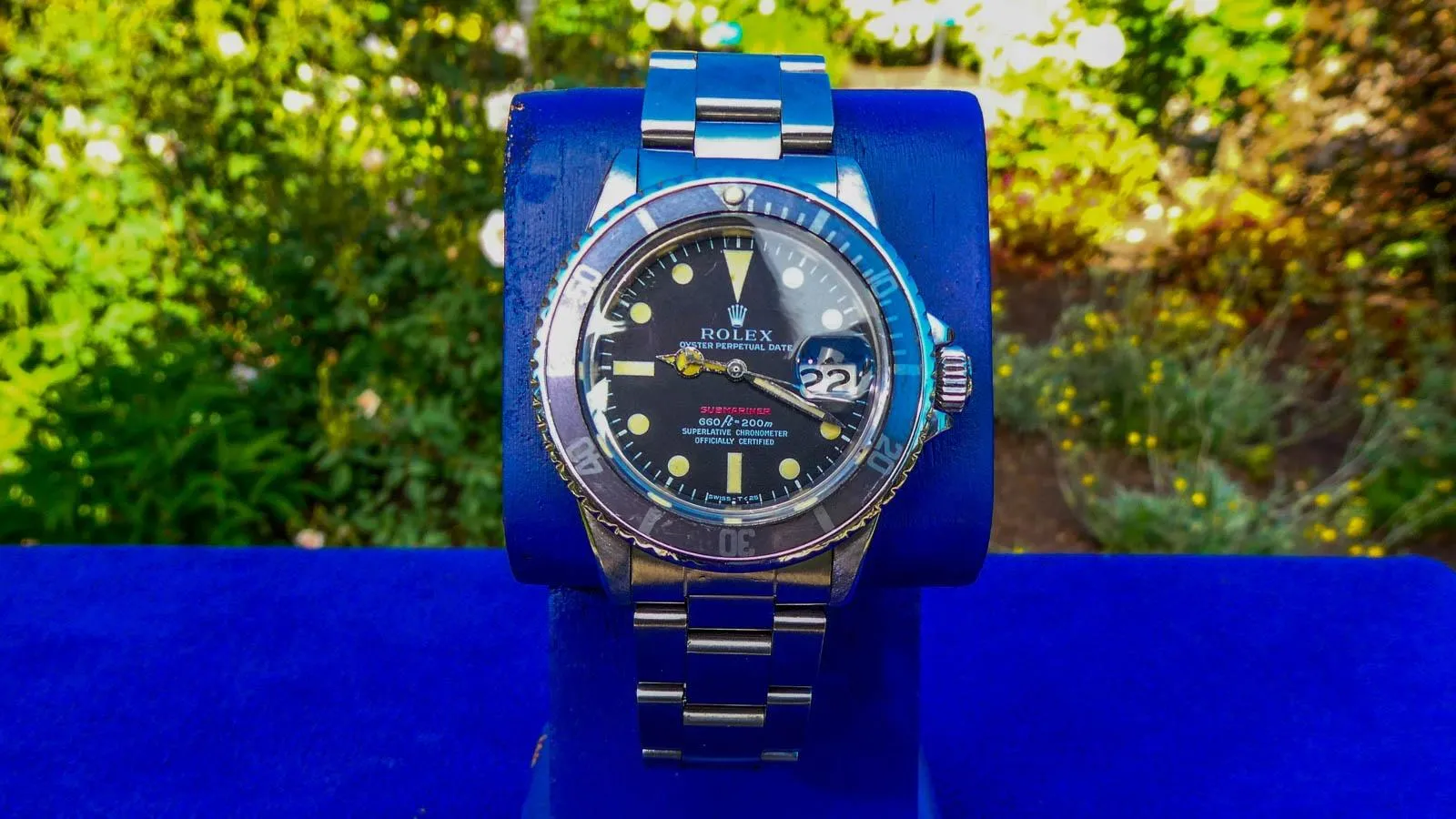 Close up of a 1970 Rolex "Red" Submariner Watch on a blue watch stand
