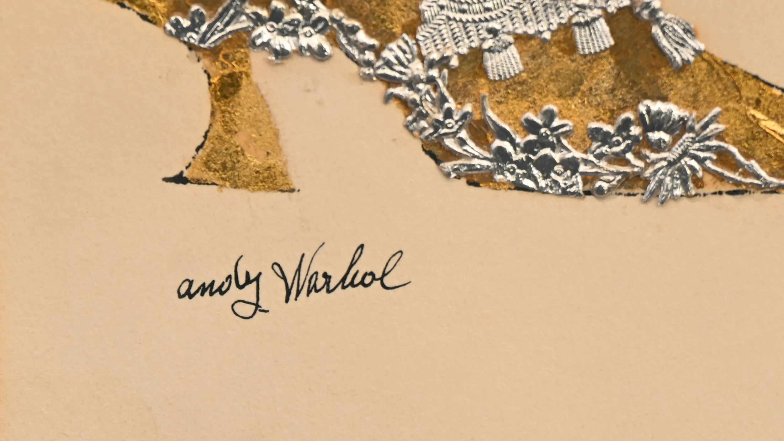 Close up of an ink signature that reads "andy warhol." Above the signature is a collage of a gold painted shoe and with a lace trim