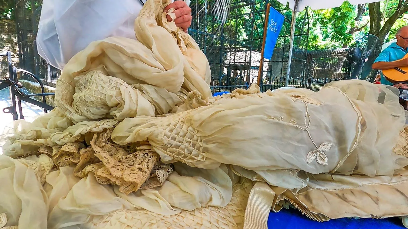 Appraiser touching a a silk dress that has smocked details, lace trim, embroidered vine designs, and a long train.