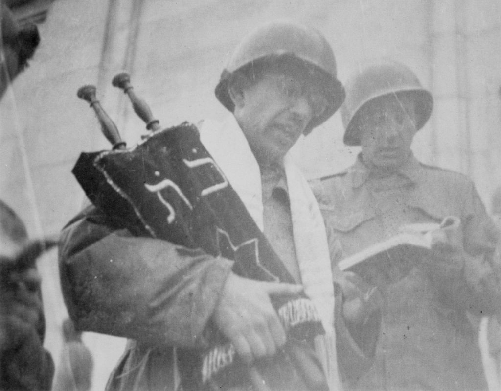 Rabbi Chaplain David Max Eichhorn holding a torah saved in France and performing a Jewish service in the Zeppelin Stadium in Nuremburg, Germany. April, 1945.
