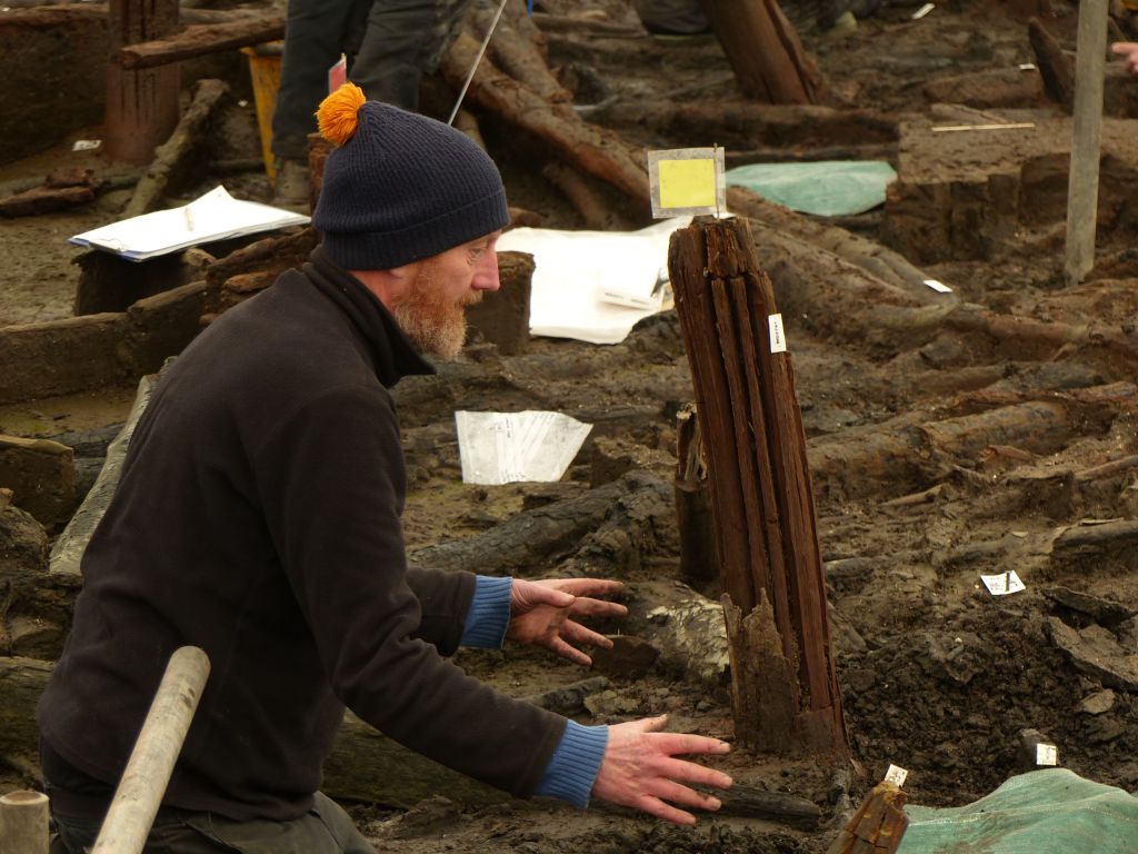 Mark Knight kneeling with his hands gesturing about a post in the ground.